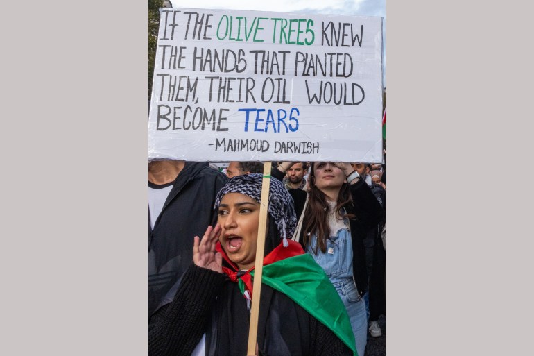 A pro-Palestinian protester holds a sign bearing a quotation by Palestinian poet Mahmoud Darwish during a march through central London
