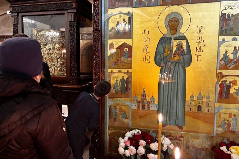 A boy leans forward to kiss the icon of Saint Matrona featuring Stalin inside Tbilisi's Sameba Cathedral [Al Jazeera]