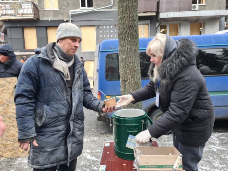 A voluntária Svitlana Stetsenko entrega uma xícara de mingau a um funcionário de emergência próximo a um prédio no centro de Kharkiv destruído por mísseis russos- 1706525721