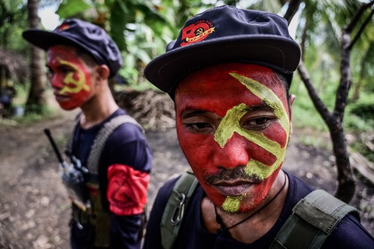 Fighters from the New People's Army mark the griup;s 5th year. They are in a jungle-like location. They've painted their faces red with a golden hammer and sickle