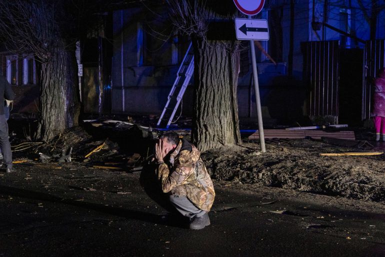 A man squats down and holds his head in his hands after a Russian air attack on Kharkiv. He is out on the street in the darkness.
