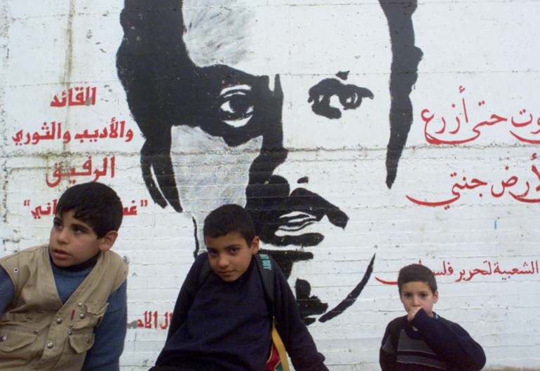 Palestinian refugee school children sit by a wall painting featuring Palestinian writer Ghassan Kanafani, killed in the '70 by Israelis, in the Dheisheh refugee camp in the outskirts of Bethlehem January 4, 2001.