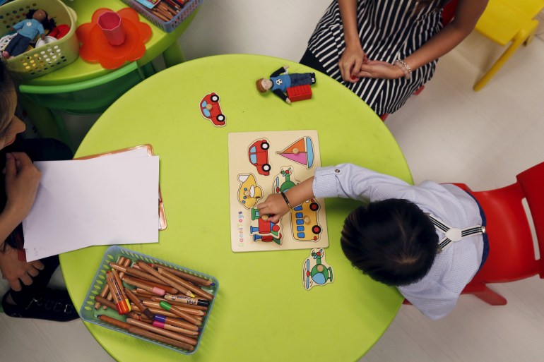 Ein Kleinkind sitzt an einem runden Tisch und identifiziert die vor ihm platzierten Gegenstände