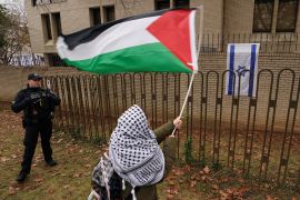 A policeman watches as a demonstrator waves a Palestinian flag outside the Israeli embassy in Washington, DC, December 1, 2023 [File: Kevin Lamarque/Reuters]