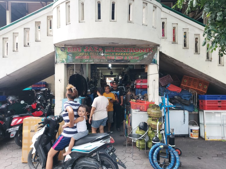 The exterior of the Notoharjo Market. There is a balustrade going up. There are people outside including a woman on a motorbike with a toddler on the back