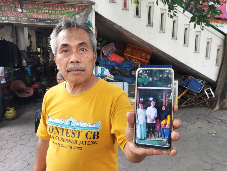 Edy Saryanto holds up his mobile phone to show a picture of him with vice presidential hopeful and mayor of Solo, Gibran Rakabuming Raka. Edy is standing outside the market