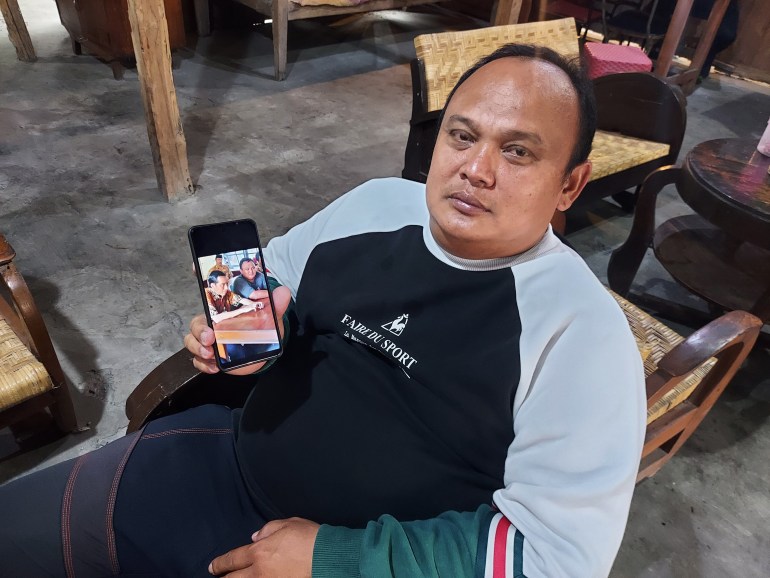 Рыночный трейдер Фири Сетиаван сидит на стуле, держит телефон и показывает свою фотографию с Джокови.