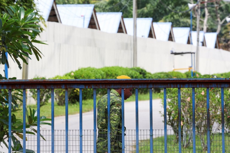 Exterior appearance of Bidor Detention Centre.  There is a high fence and a gate.  A security guard stands at the gate. 
