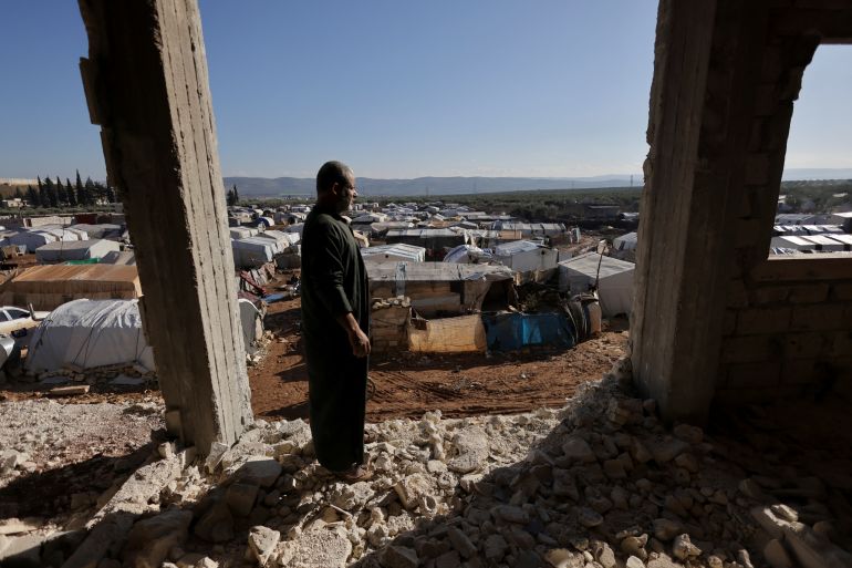 Amer Mohammed Haleel, a 50-year-old quake survivor, poses as he stands inside a damaged building that housed his apartment and was struck by last year's deadly earthquake on February 6, 2023, overlooking a tent camp where he lives with his family, in the rebel-held town of Jandaris, Syria January 24, 2024. REUTERS/Khalil Ashawi