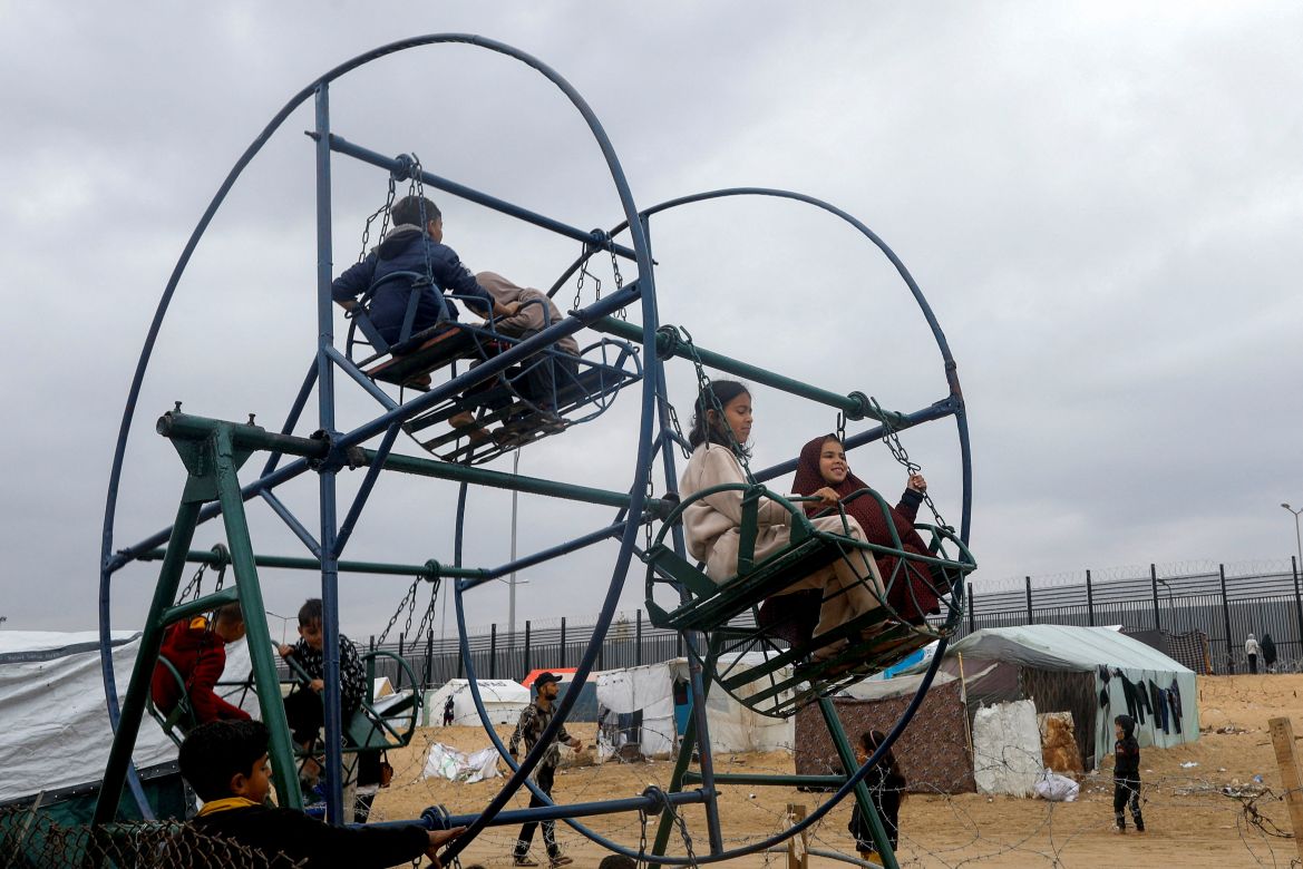 Displaced Palestinian children, who fled their houses due to Israeli strikes, amid the ongoing conflict between Israel and the Palestinian Islamist group Hamas, play on swings at a tent camp at the border with Egypt, amid fears of an Israeli ground assault in Rafah, in the southern Gaza Strip February 18