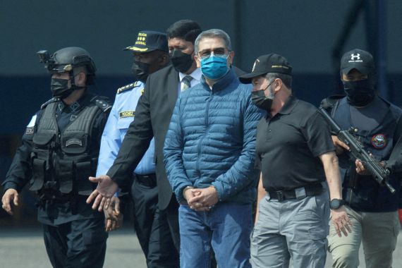 Juan Orlando Hernandez, wearing a face mask and sunglasses, walks in the custody of US federal agents.