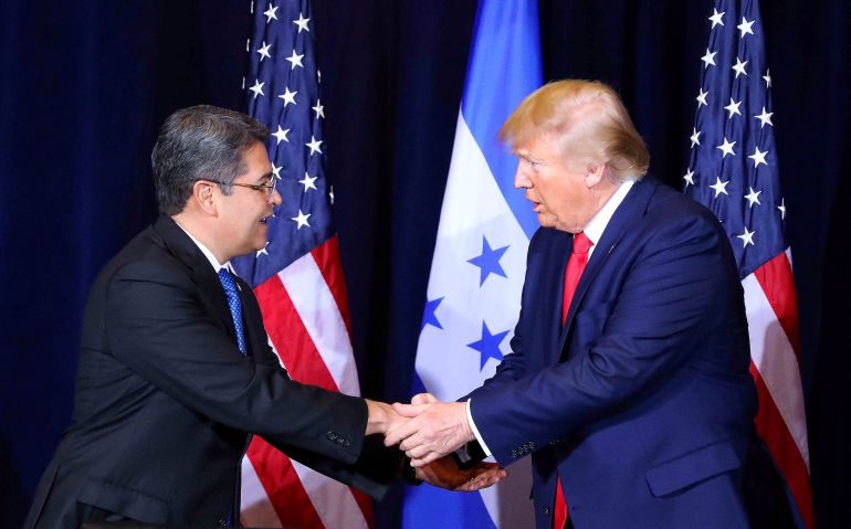 Donald Trump shakes hands with Juan Orlando Hernandez, in front of a row of flags.
