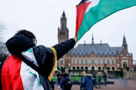 A man waves a Palestinian flag as people protest on the day of a public hearing held by The International Court of Justice (ICJ) to allow parties to give their views on the legal consequences of Israel&#039;s occupation of Palestinian territories before eventually issuing a non-binding legal opinion, in The Hague, Netherlands, February 21, 2024. [Piroschka van de Wouw/Reuters]