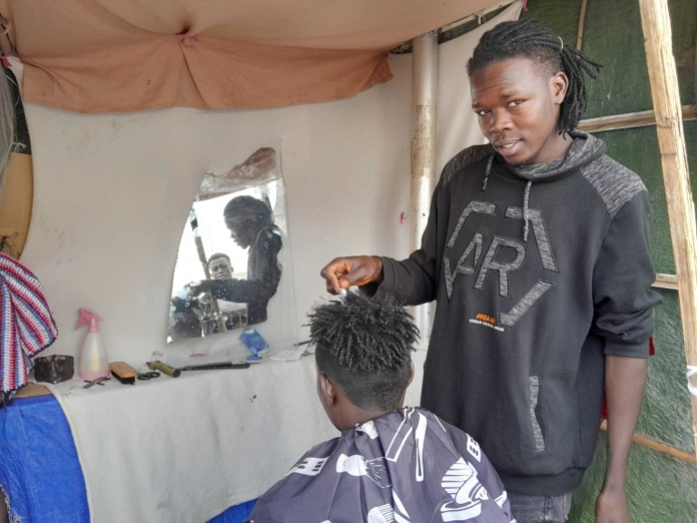 A barber styling a client's hair in a makeshift tent