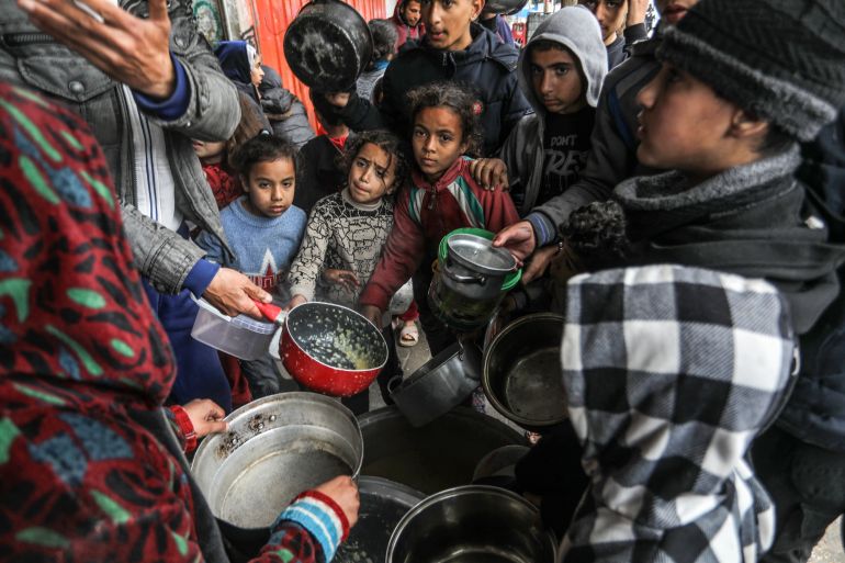 Palestinians holding empty bowls receive food distributed by volunteers of charities as people facing hunger crisis and famine risk due to the Israeli embargo imposed on the territory, in Rafah, Gaza on February 18