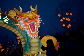 A dragon lantern lit up at night. People are walking nearby.