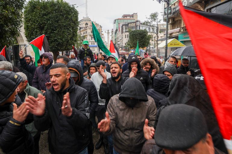 people wearing dark coloured clothes protest holding palestinian flags