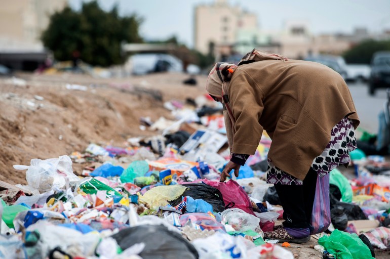 A woman digs through garbage in Kasserine, Tunisia