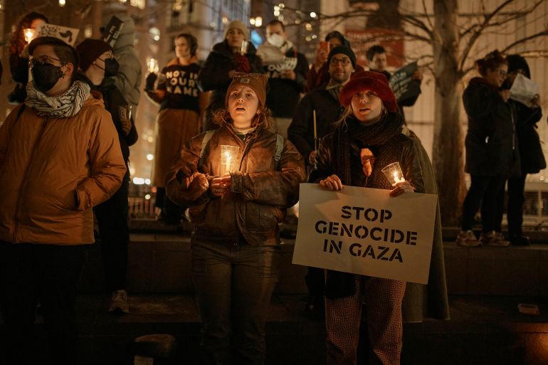 Protesters hold candles and raise signs that read "Stop Genocide in Gaza" outside in New York.