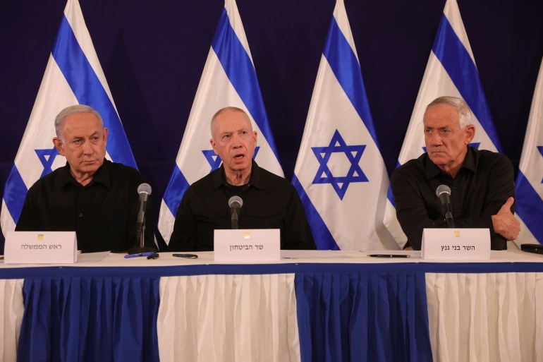 three men wearing black sit in front of Israeli flags