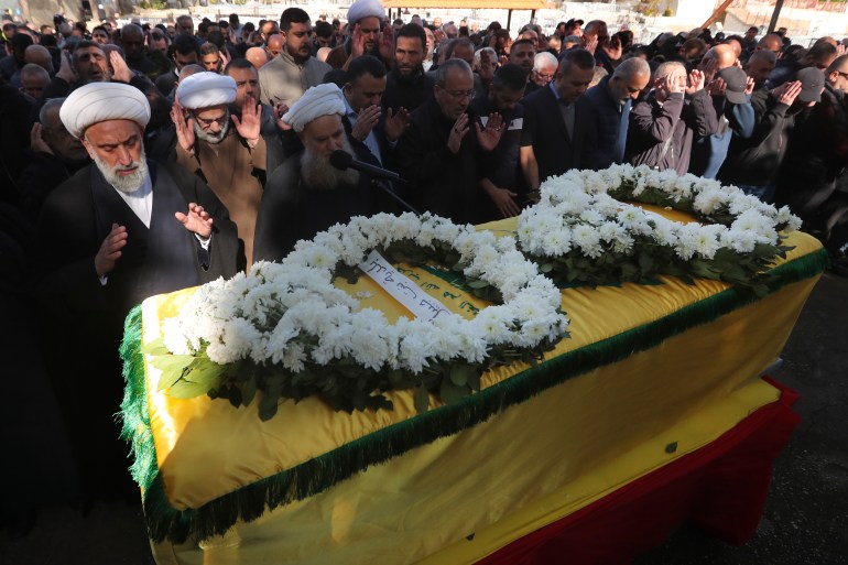Mourners pray in front of a coffin draped in yellow with white wreaths