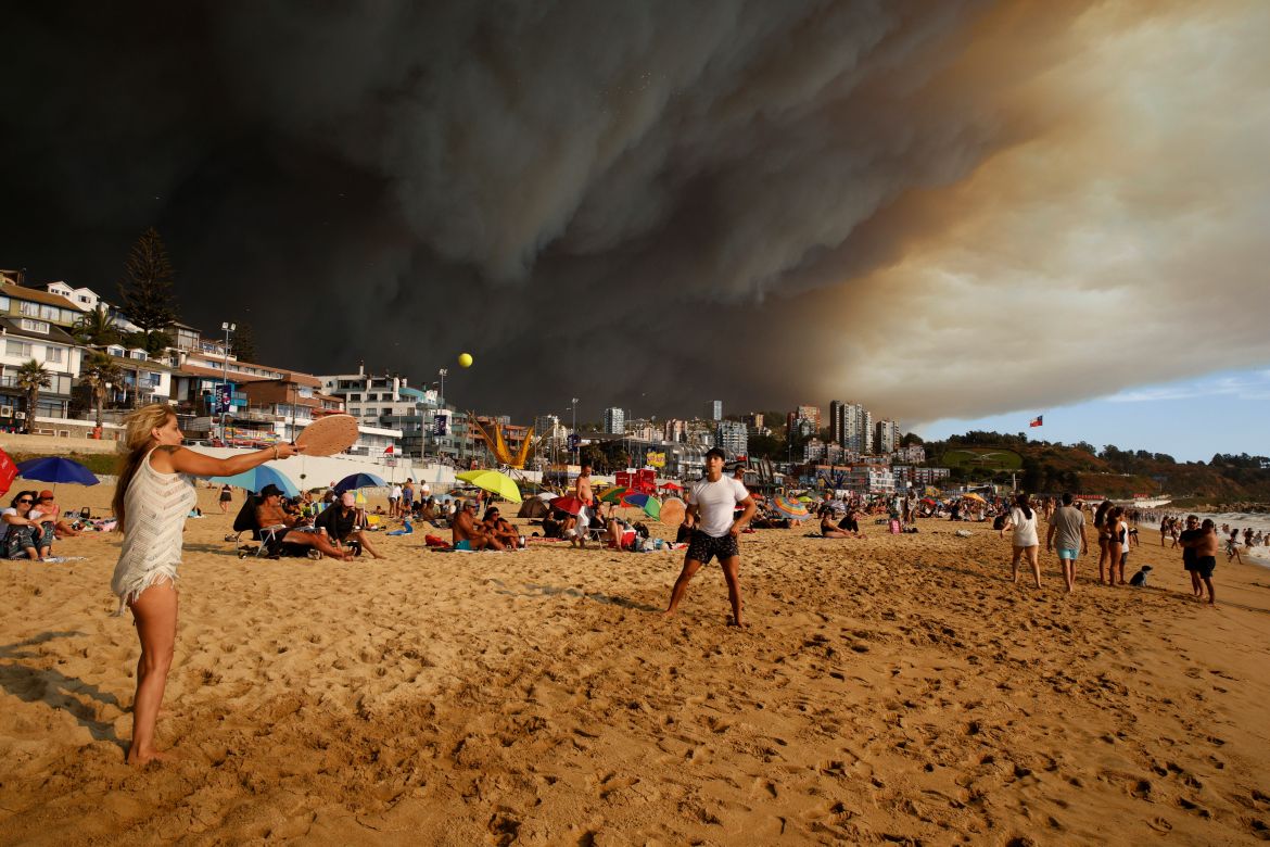 Vacationers play paddle ball on a beach backdropped by a darkening sky caused by smoke from nearby forest fires, in Viña del Mar, Chile, Friday, Feb. 2