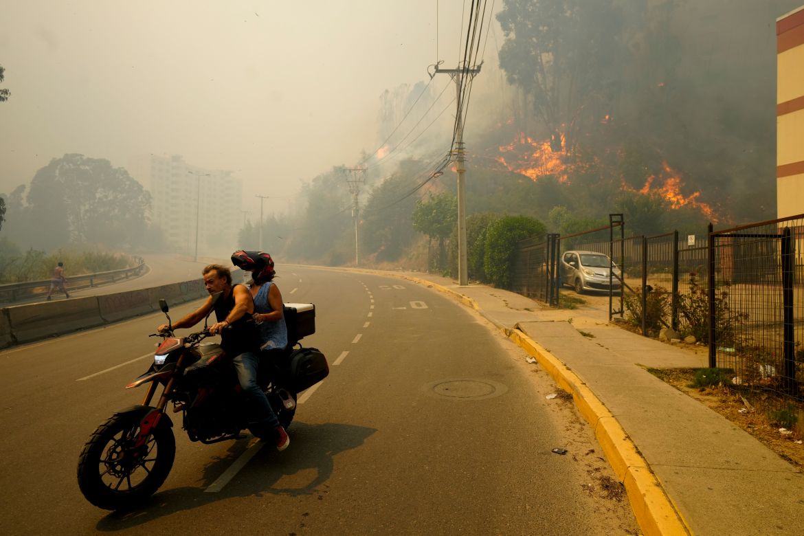 Residents evacuate on a motorcycle as smoke caused by forest fires fill the sky and flames spread into Vina del Mar,