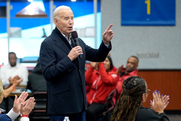 Joe Biden speaks into a handheld microphone and lifts a finger in gesture at a campaign stop.