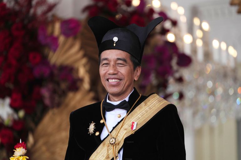 Joko Widodo. He is weaaring a traditional outfit for royalty from central Java. with a white shirt, black bow tie, black jacket and gold sash. He is also wearing a black hat with extensions like ears on either side.