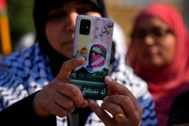 A demonstrator takes photos with her mobile phone covered with a picture of Abu Obeida, the spokesman for the Qassam Brigades, the Hamas' military wing, during a protest to demand a ceasefire and support Palestinians in the Gaza Strip, near the headquarters of U.N. Economic and Social Commission for Western Asia (ESCWA) in Beirut, Lebanon, Sunday, Feb. 11, 2024. The Arabic words read: " Al-Aqsa flood." (AP Photo/Bilal Hussein)
