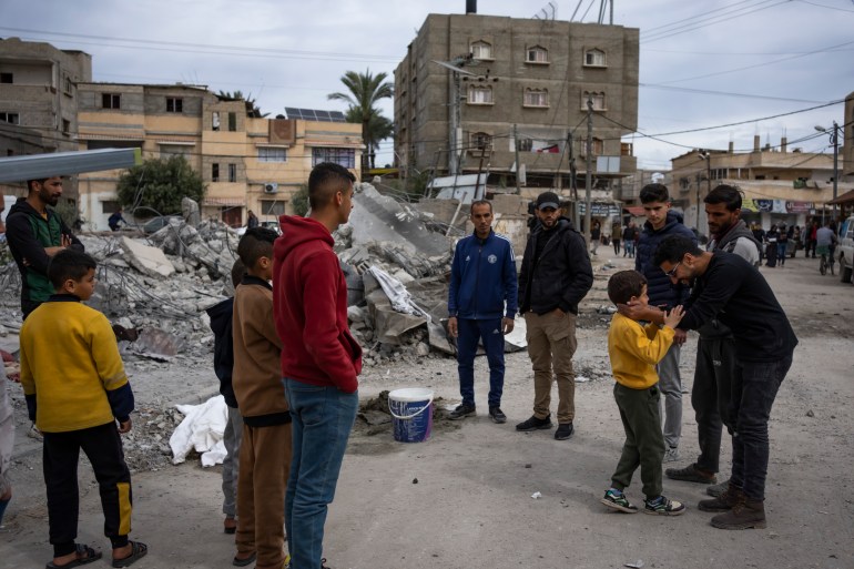 Ibrahim Hasouna, right, the sole survivor among his family, stands in front of the rubble of his family house with his friends