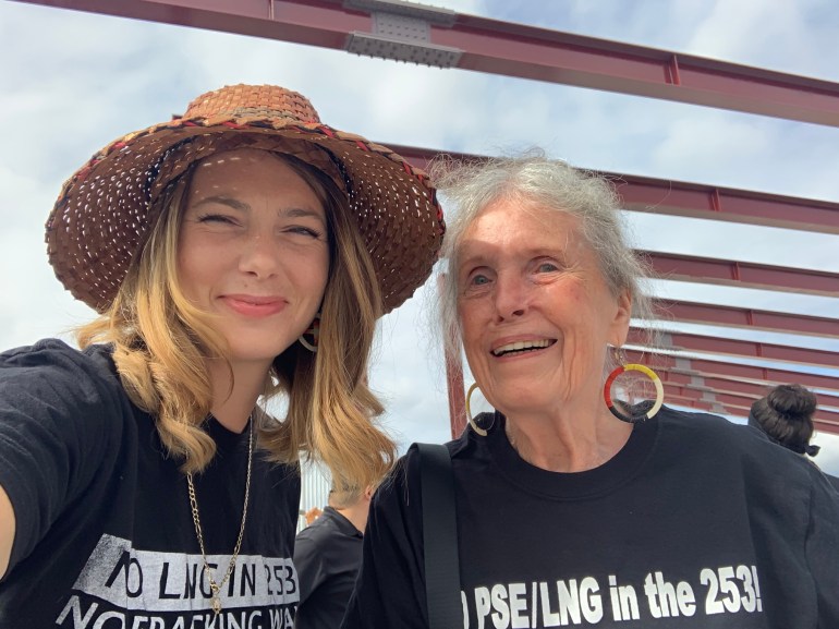 Amber Taylor, com um chapéu de tecido e uma camiseta protestando contra o gasoduto de GNL, está ao lado de sua avó Ramona.