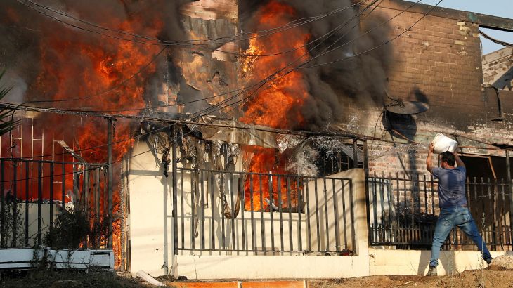 Man throwing bucket of water onto burning house.