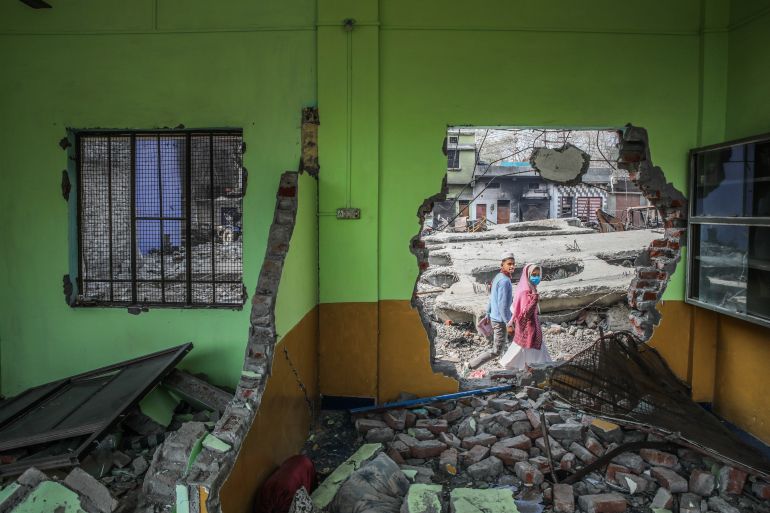 A young Muslim boy and girl walk past a hole in the wall of a madrasa demolished in the north Indian city of Haldwani, on February 9, 2024, the day after the demolition [Arbab Ali/Al Jazeera]