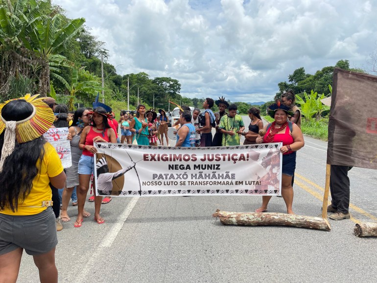 Os manifestantes erguem uma faixa e ficam na estrada para pedir justiça pela morte a tiros de um líder indígena.