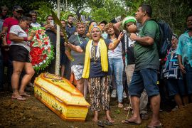 Indigenous activists from the Pataxó Hã-Hã-Hãe community protest in front of a coffin in a forested part of Brazil.