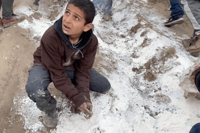 A Palestinian child tries to pick up spilled flour during aid distribution in north Gaza. [Screengrab/Al Jazeera]
