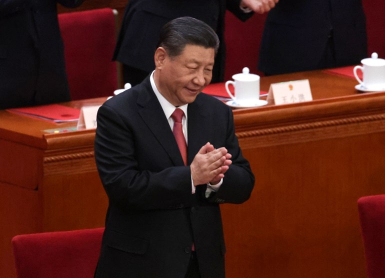 Xi Jinping standing and clasping his hands together, He is on stage at the National People's Congress,