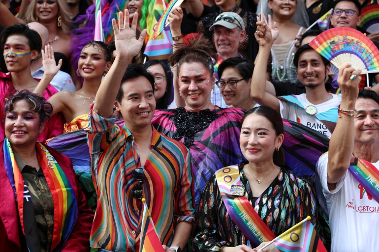 Move Forward Party's former leader Pita Limjaroenrat and Pheu Thai's Paetongtarn Shinawatra taking part in 20203's Pride parade. Pita is wearing a shirt swirled with the colours of the rainbow. Paetongtarn is wearing a rainbow sash. They are smiling and Pita is waving.