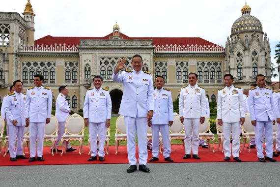 Members of the Thai cabinet pose on the steps of government house. They're wearing traditional white outfits and standing on a red carpet. Prime Minister Srettha Thavisin is in front and waving.