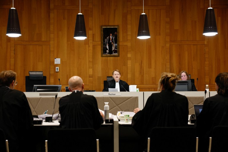 Um tribunal nos Países Baixos que julga um caso relacionado com exportações militares.  A sala tem painéis de madeira e há um retrato na parede. 