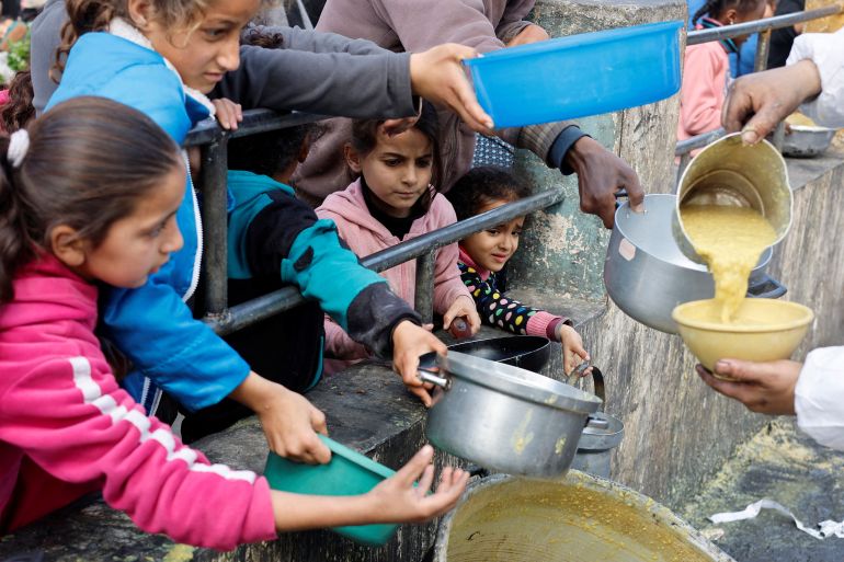 Palestinian children wait to receive food cooked by a charity kitchen