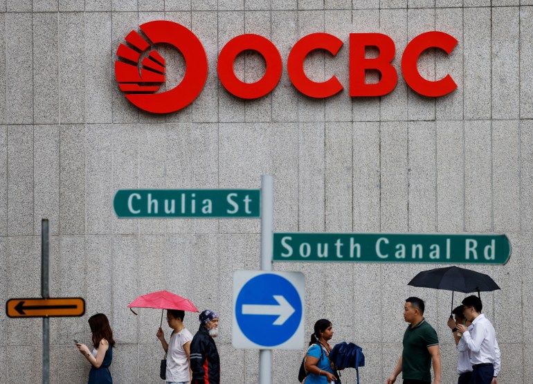 An exterior of OCBC Bank in SIngapore with people walking past. They are holding umbrellas.