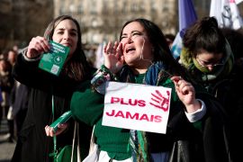 A woman holds a placard which reads "Never again" as they gather to watch on a giant screen French lawmakers gathered for a special Congress in Versailles to vote on a bill to include the right to abortion into the French constitution