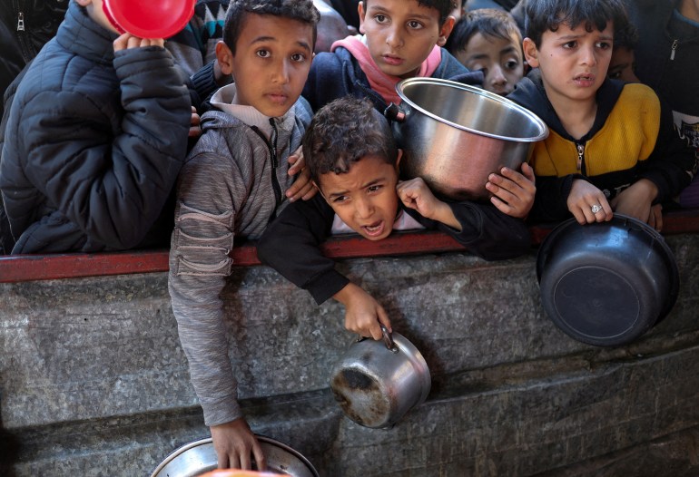 Palästinensische Kinder warten in Rafah auf Essen, das von einer Wohltätigkeitsküche zubereitet wird, während die Nahrungsmittelknappheit herrscht, während der anhaltende Konflikt zwischen Israel und der palästinensischen islamistischen Gruppe Hamas anhält