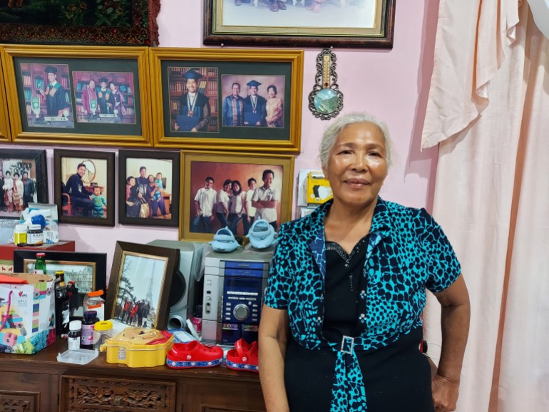 Panjaitan stands in front of photographs of her son Siregar which she has hung on the wall of her home.