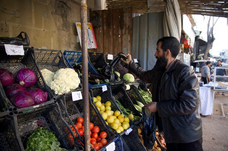 Nazik, sakallı bir adam olan Halid, pazardaki basit bir tezgâhtan sebze seçiyor