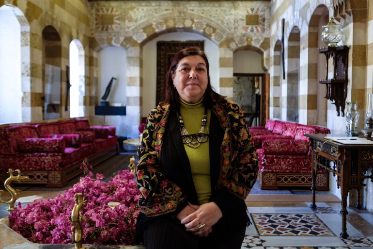 Olfat Baba sits in a mamluk style room with burgundy divans behind her