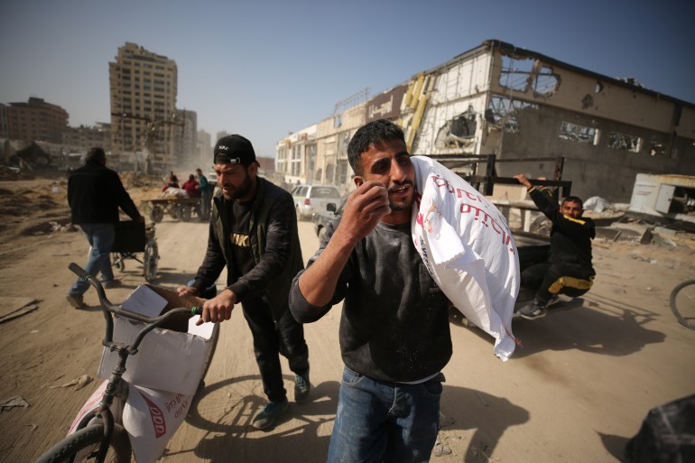 Palestinians, who are unable to meet their basic needs due to the Israeli army's obstruction of humanitarian aid, receive a bag of flour from an aid truck that arrived at al-Rashid Street