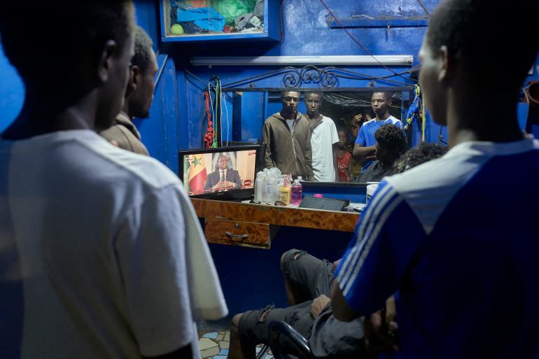 As pessoas assistem ao presidente do Senegal, Macky Sall, na TV durante uma conferência de imprensa ao vivo.